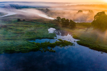 Bright golden sun rays in thick fog. Blue river in countryside. Temperature drop concept