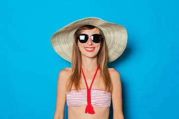 Young woman in a swimsuit, glasses and a wide-brimmed hat on a blue background. Concept of vacation, summer, vacation at sea