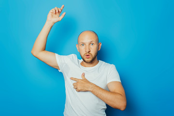 Young man in a white T-shirt with wet armpits from sweat on a blue background. Concept of excessive...