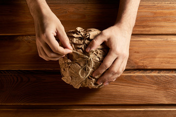 Man's hands unpack a paper bag with fresh bread. Wooden background.