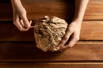 Men's hands open fresh bread packed in a paper bag. Wood background.