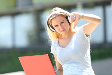 Student with laptop and earbuds gesturing thumbs down