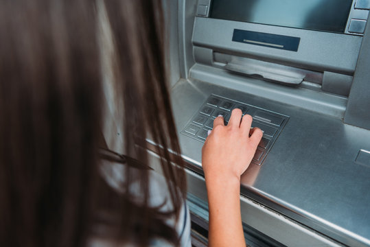 cropped view of woman entering pin code on atm machine