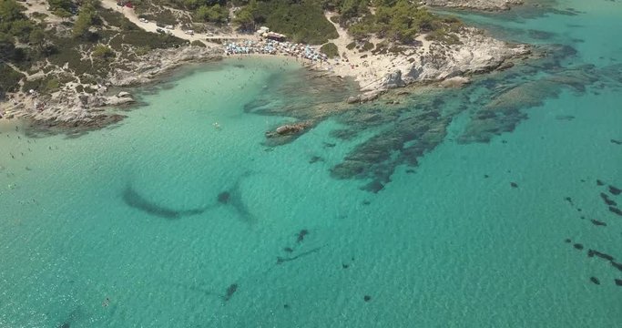 Aerial view of small beach with turquoise water next to rocks and trees in the area of Agia Paraskevi Halkidiki, Greece. View from drone