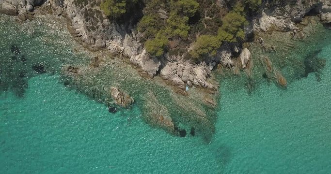 Aerial view of small beach with turquoise water next to rocks and trees in the area of Agia Paraskevi Halkidiki, Greece. View from drone