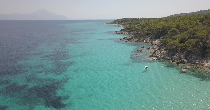Aerial view of small beach with turquoise water next to rocks and trees in the area of Agia Paraskevi Halkidiki, Greece. View from drone