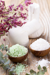 Sea salt in bowl, aroma oil in bottles, Wellness and flowers on grey textured background and flowers on vintage wooden background. Selective focus.