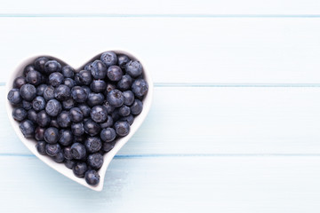 Fresh blueberries, in a heart shaped bowl on a wooden background.