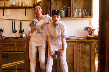 two young stylish nurses in medical costumes are standing with cups and smiling on the wooden kitchen background with sunshine. two girls doctors. medical concept, free space