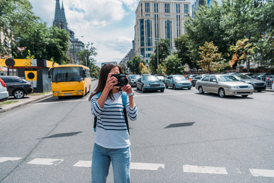 young woman taking photo while standing on street with cars
