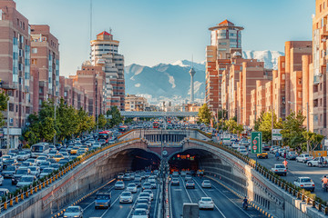 06/05/2019 Tehran,Iran,Famous view of Tehran,Flow of traffic inside, above and nearby round Tohid Tunnel with Milad Tower and Alborz Mountains in Background - obrazy, fototapety, plakaty