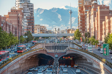 06/05/2019 Tehran,Iran,Famous view of Tehran,Flow of traffic inside, above and nearby round Tohid Tunnel with Milad Tower and Alborz Mountains in Background - obrazy, fototapety, plakaty