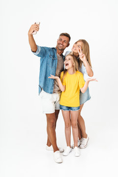 Full length photo of joyful woman and man with little girl smiling while taking selfie on cellphone