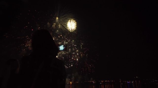 Silhouette of a girl with a smartphone on the background of bright colorful fireworks in the black sky.