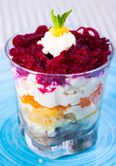 verrin glass with Russian salad herring under fur coat from vegetables on blue plate