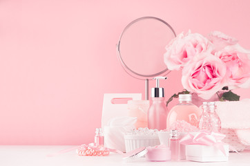 Spa cosmetics products, round mirror, roses in pastel pink and silver color - cream, bath salt, essential oil, soap, bottle, bowl, towel on white wood shelf.