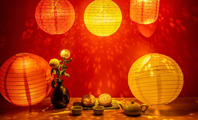 Mid-Autumn mooncakes and tea under colorful lantern lights in red background
