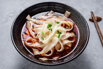 A bowl of nutritious and delicious red oil knife noodles on a cement texture background
