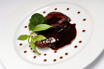 Delicious grilled meat thigh on white plate with soy sauce in center of dish, view from above, close-up