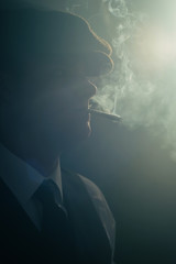Retro man with cap smokes cigarette in smoky room. Side view.