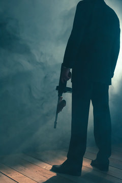 Retro gangster stands with machine gun in smoky room. Rear view.