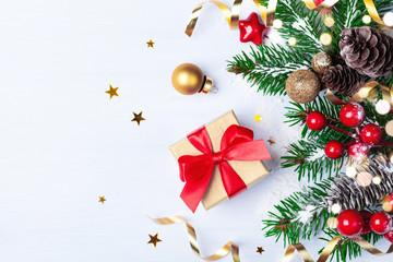 Golden gift or present box, snowy fir branches, conifer cones, Christmas decoration and red berry on white table top view.