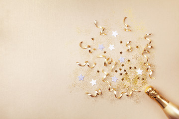 Champagne bottle with confetti stars, glitter and party streamers on golden background. Christmas,...