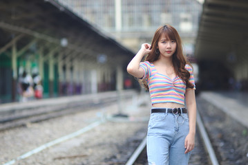 A photograph of a beautiful Asian woman standing on the railroad.