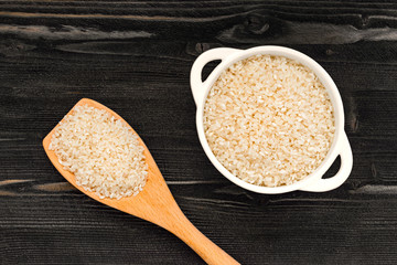 cereal dry rice in white bowl and spoon  on dark wooden desk surface