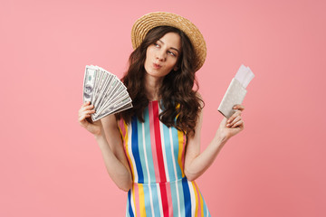 Thinking young cute woman posing isolated over pink wall background holding passport with tickets.