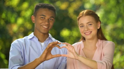 Cute teenagers making heart sign with hands and looking into camera, affection