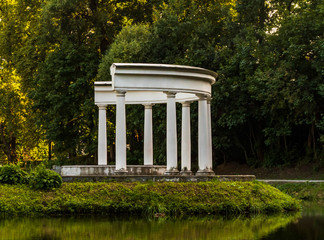 A small building with white columns on the greenery of the park