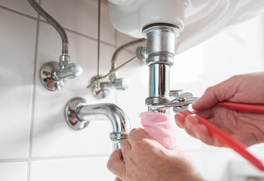 man repairing sink trap with adjustable pipe wrench in bathroom