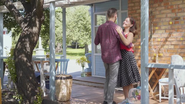 Young happy man and woman dancing on the porch of the old house smiling. Adorable couple having fun together. Leisure at home. Tender relationship.