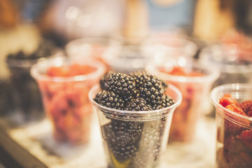 Close up of blackberries in plastic glass. Raspberries in the background at street market stand.
