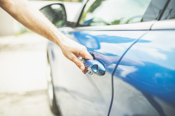 Close up of man opening door of blue vehicle.