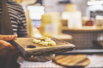 Close up of man holding wooden board with cheese at agricultural fair at street stand.