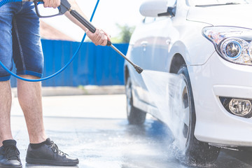 Modern man washing car with high pressure car washer spray gun
