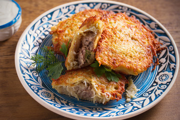 Potato Pancakes Filled With Meat. Vegetable fritters stuffed with meat on blue plate and sour cream or yogurt