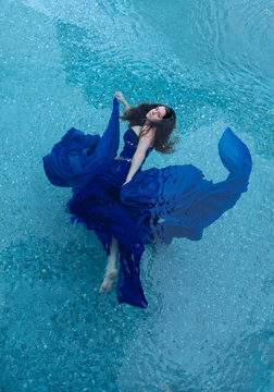 beautiful young woman in blue evening dress floating weightlessly elegant in the water