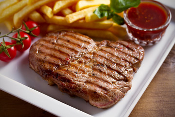 Grilled pork steak with fries, sauce and vegetables on white plate