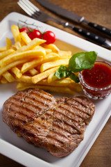 Grilled pork steak with fries, sauce and vegetables on white plate
