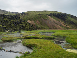 View on geothermal area with natural hot spring, thermal baths in Landmannalaugar camp site, Iceland. Grass meadow, lava fields and mountains in background
