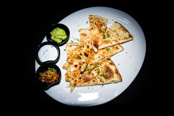 a traditional chicken quesadilla filled with cheese and accompanied with a trio of dips