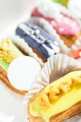 many tasty multi-colored eclairs lie in a box on a wooden table