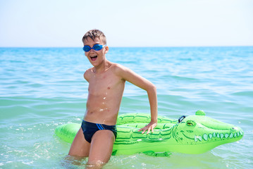 BOY OF TEENAGERS IN WATER GOGGLES SWIMS ON THE INFLATABLE TOY CROCODILE.