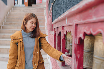Beautiful young asian woman in yellow jacket rotating praying wheels for religious reason at...