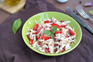 Salad of white cabbage, boiled chicken, red sweet pepper and brown beans in a green bowl on a brown concrete background. Healthy food.