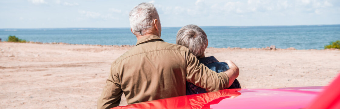 panoramic view of senior couple of tourists standing near car and embracing at beach - Powered by Adobe