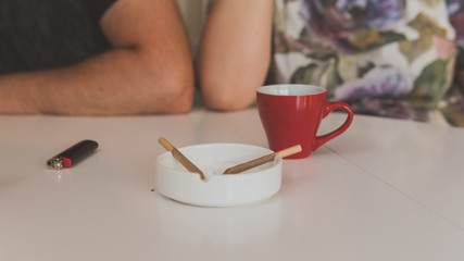 Two medical marijuana joins are in the ashtray, a cup of coffee and lighter near. Smoking marijuana joint indoors.